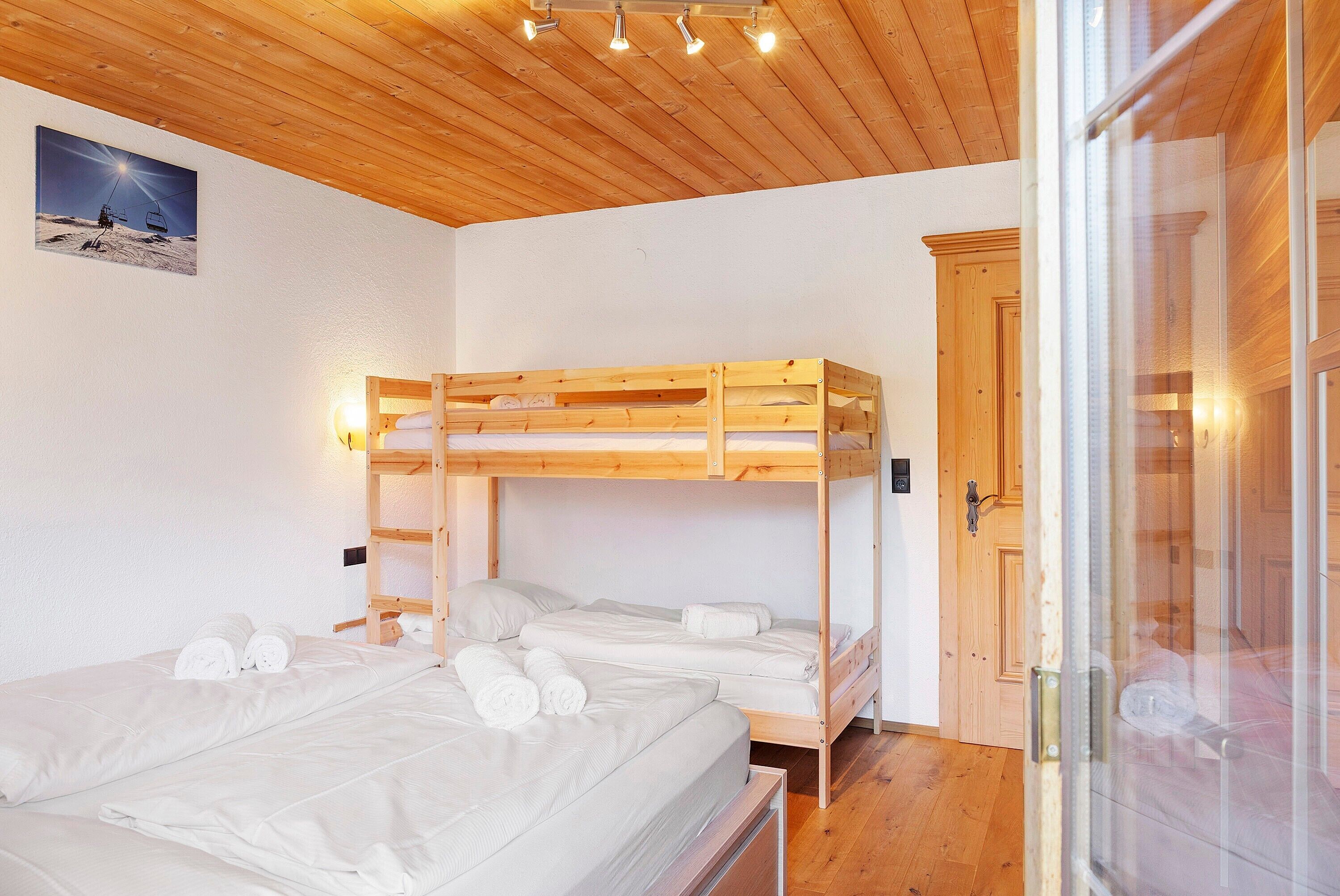 Ein Zimmer mit Etagenbetten, einer Holzbalkendecke, einem gerahmten Bild an der Wand und einer Tür mit Glasfenster.