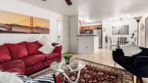A modern living room with a red sofa, a black sofa, and a glass coffee table. There is a kitchen in the background with wooden cabinets and a microwave. - Cordillera Condo: Pools, Hot Tubs & Racquetball | Patio Retreat (Phoenix)