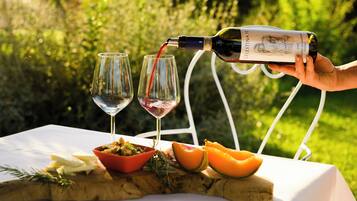 A bottle of wine being poured into two glasses on a table with food and a wooden board.