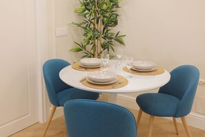 A dining table set with plates, cutlery, and glasses, surrounded by blue chairs, with a bamboo plant in the background. - Sofia Suites &Rooms (Pompei)