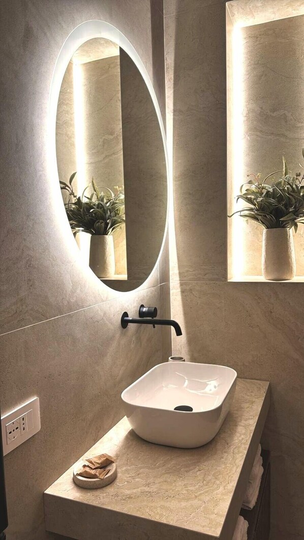 Un bagno con un ampio specchio ovale, un lavabo rettangolare e due piante in vaso.