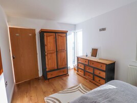 Un dormitorio con un armario de madera, una cómoda, una cama y una ventana con luz natural.