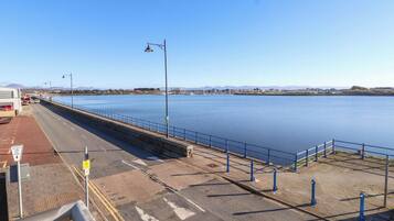 A waterfront promenade with a paved walkway, a metal railing, and a clear view of the water.