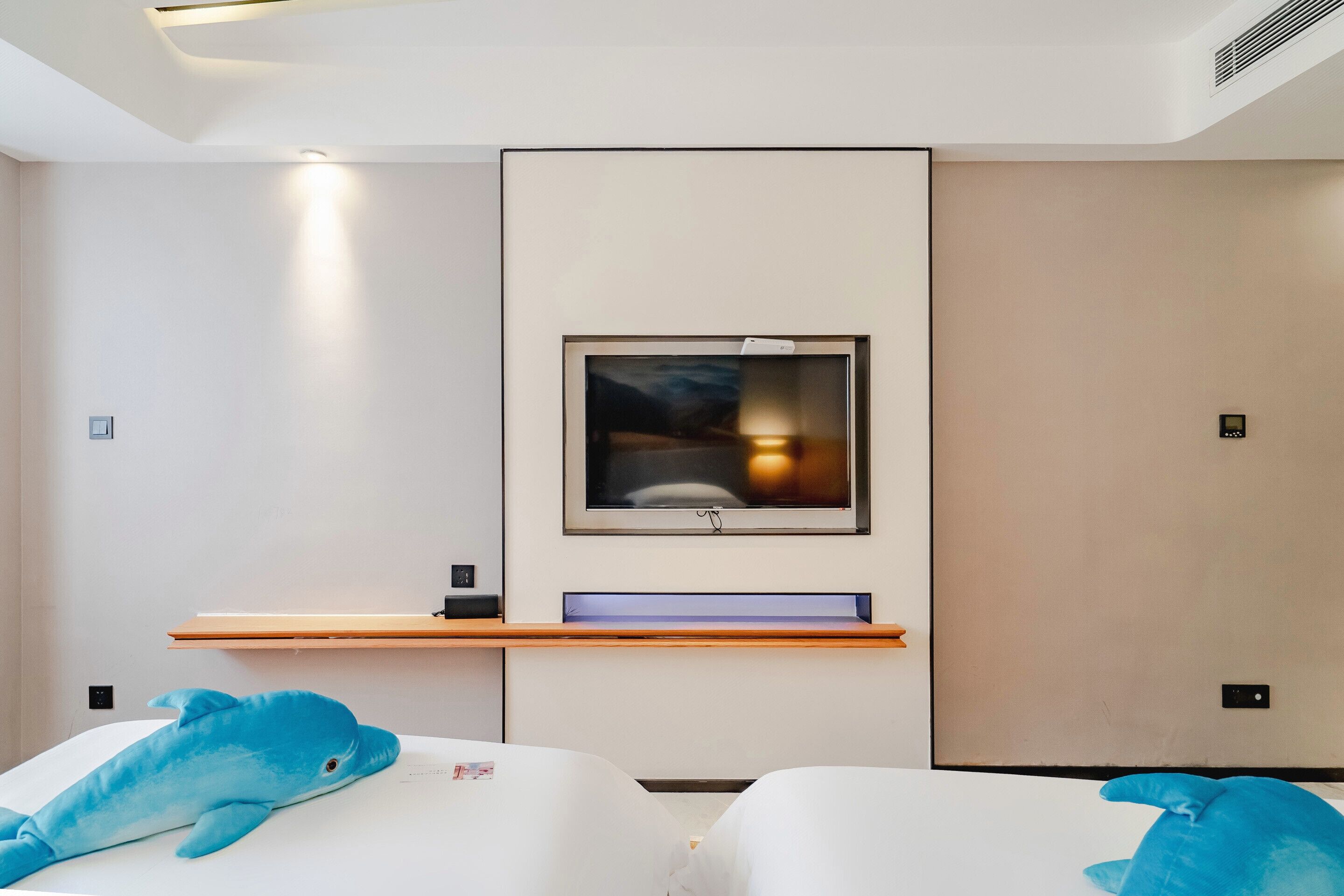 Une chambre d’hôtel moderne équipée d’un lit, d’un téléviseur fixé au mur et d’une étagère en bois.