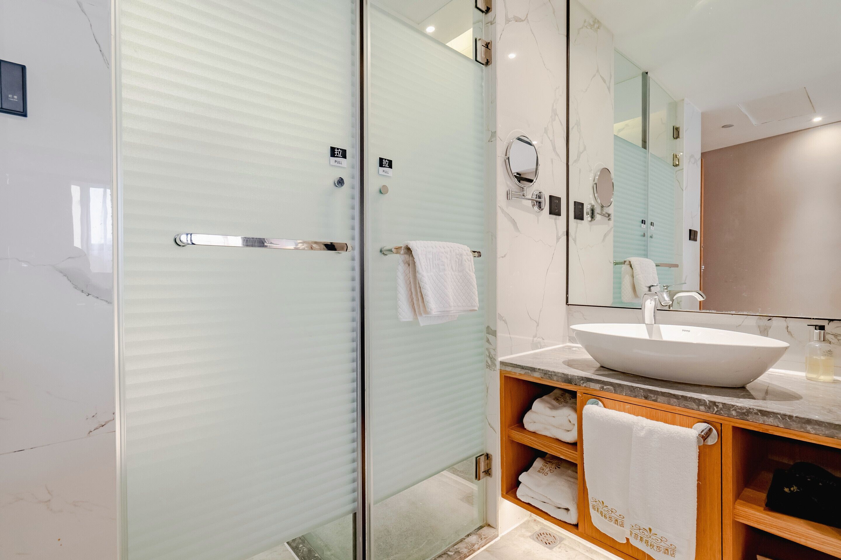 A modern bathroom with a glass-enclosed shower, a large mirror, and a marble countertop with a sink.