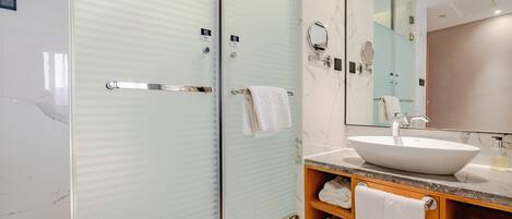 A modern bathroom with a glass-enclosed shower, a large mirror, and a marble countertop with a sink.