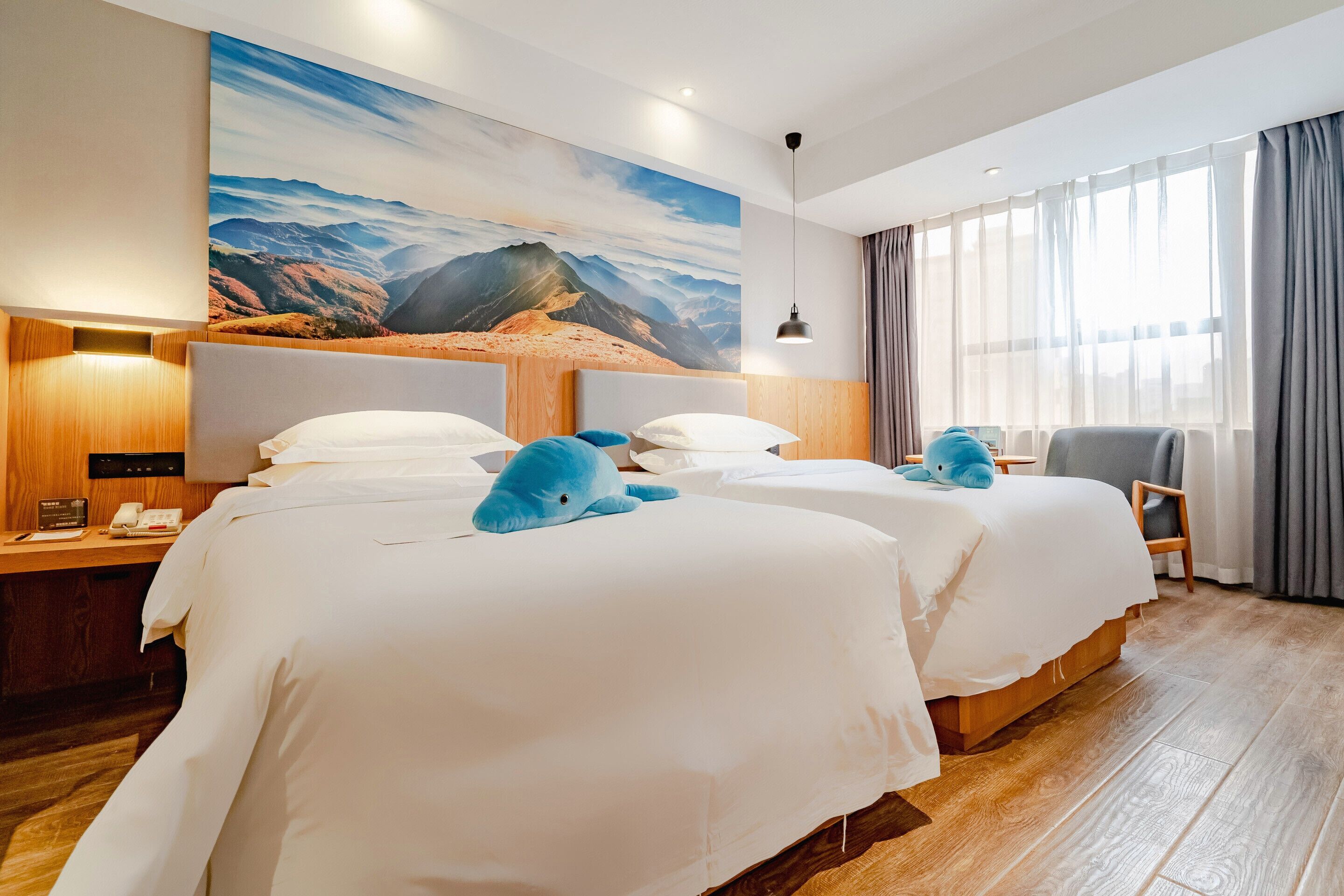 Une chambre d’hôtel avec deux lits, un grand tableau représentant un paysage de montagne, un bureau avec une lampe et une chaise.