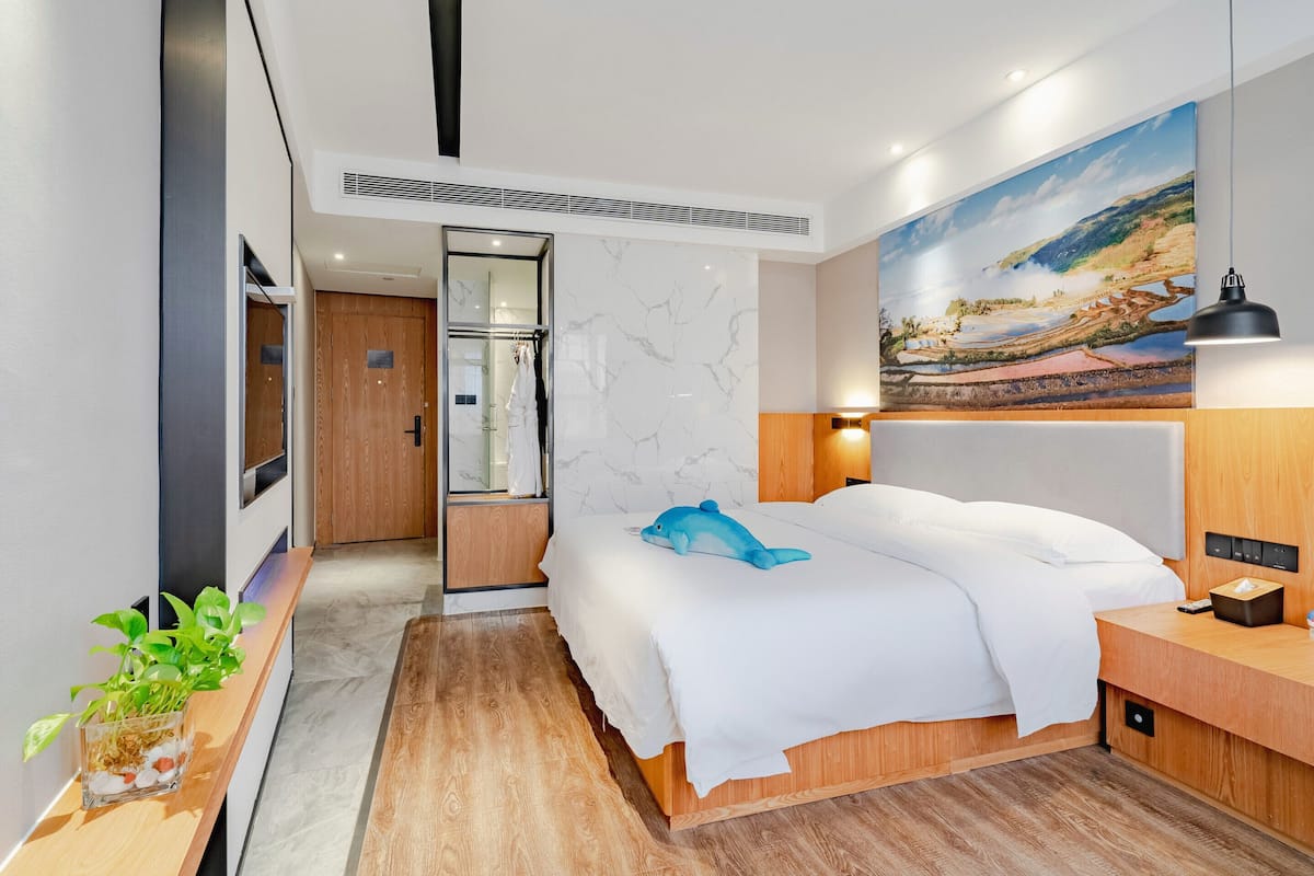 Een moderne hotelkamer met een bed, een houten nachtkastje, een wandlamp, een schilderij en een pot met een plant.