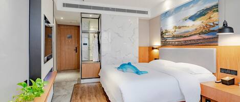 A modern hotel room with a bed, a wooden nightstand, a bedside table, a wall-mounted lamp, a painting, and a potted plant.