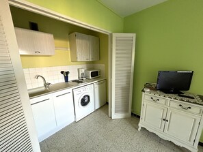 A compact kitchen with a washing machine, microwave, and a television on a table.