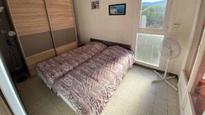 A bedroom with a bed, a wardrobe, a window with a view, and a standing fan. - Beachfront apartment for 4 with loggia in Argelès-sur-Mer (Argelès-sur-Mer)