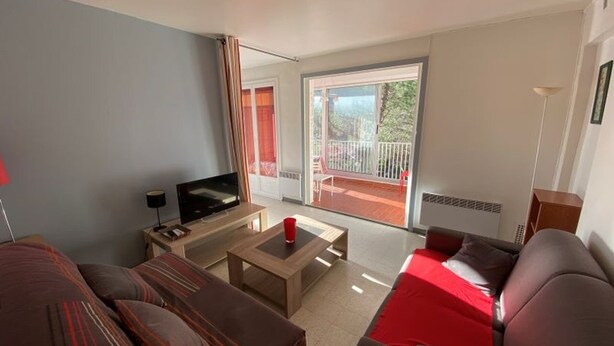 A modern living room with a flat-screen TV, a coffee table, and a sofa. There is a balcony with a red chair and a view of greenery. - Beachfront apartment for 4 with loggia in Argelès-sur-Mer (Argelès-sur-Mer)