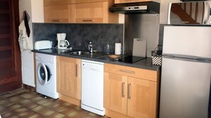 A compact kitchen with wooden cabinets, a washing machine, a dishwasher, a coffee maker, and a refrigerator. - Mezzanine apartment for 4 near beach (Argelès-sur-Mer)