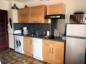 Eine kompakte Küche mit Holzausstattung, einer Waschmaschine, einem Geschirrspüler, einer Kaffeemaschine und einem Kühlschrank.