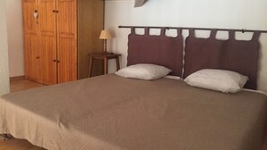 A bedroom with a bed, two pillows, a nightstand, a lamp, and a wooden wardrobe. - Mezzanine apartment for 4 near beach (Argelès-sur-Mer)