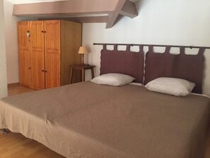 Ein Schlafzimmer mit einem Bett, zwei Kissen, einem Nachttisch, einer Lampe und einem Holzschrank.