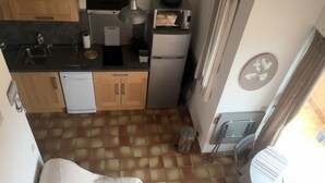 A compact kitchen with a sink, microwave, and small refrigerator. A trash can is near the door, and a chair is placed outside. - Mezzanine apartment for 4 near beach (Argelès-sur-Mer)