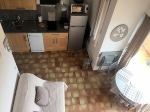 Eine kompakte Küche mit Spüle, Mikrowelle und kleinem Kühlschrank. Ein Mülleimer befindet sich in der Nähe der Tür, und ein Stuhl steht daneben.