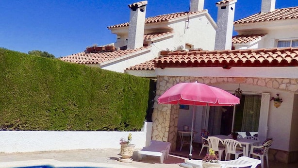 Uma área de piscina com muro de pedra, guarda-sol rosa e mobiliário para área externa.