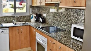 Een keuken met granieten aanrechtbladen, houten kastjes, een magnetron, een waterkoker en een vaatwasser.