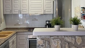 Una cocina con armarios blancos, un refrigerador de acero inoxidable, un reloj y una encimera de piedra.