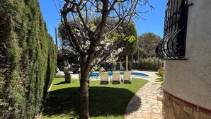 Un sendero de piedra que conduce a una zona de piscina con sillones de descanso, un césped bien cuidado y un árbol en primer plano.
