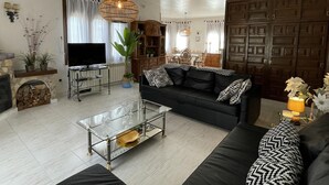 Una sala de estar con un sofá negro, una mesa de centro de vidrio, un televisor y un mueble de madera.