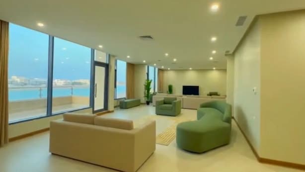 Un salón amplio con ventanas grandes, un sofá, un sillón verde y un televisor de pantalla plana.