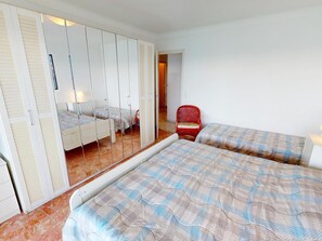 A bedroom with two beds, a red chair, and a wardrobe with mirrors. - Nice 2P with air conditioning and sea view terrace near the center (Menton)