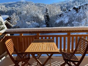 A wooden deck with a table and chairs overlooking a snowy mountain landscape. - New 78m² duplex, 2 bedrooms, pellet stove, WIFI, parking, sleeps 5 - Arâches-la-Frasse (Arâches-la-Frasse)