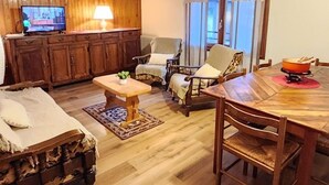 A cozy living room with wooden flooring, a television, a dining table with chairs, and a sofa. - Spacious 4-bedroom apartment with balcony and WIFI, near Châtel and La Chapelle (Abondance)