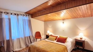 A bedroom with a wooden ceiling, a bed with multiple pillows, two bedside tables with lamps, and a chair. - Spacious 4-bedroom apartment with balcony and WIFI, near Châtel and La Chapelle (Abondance)