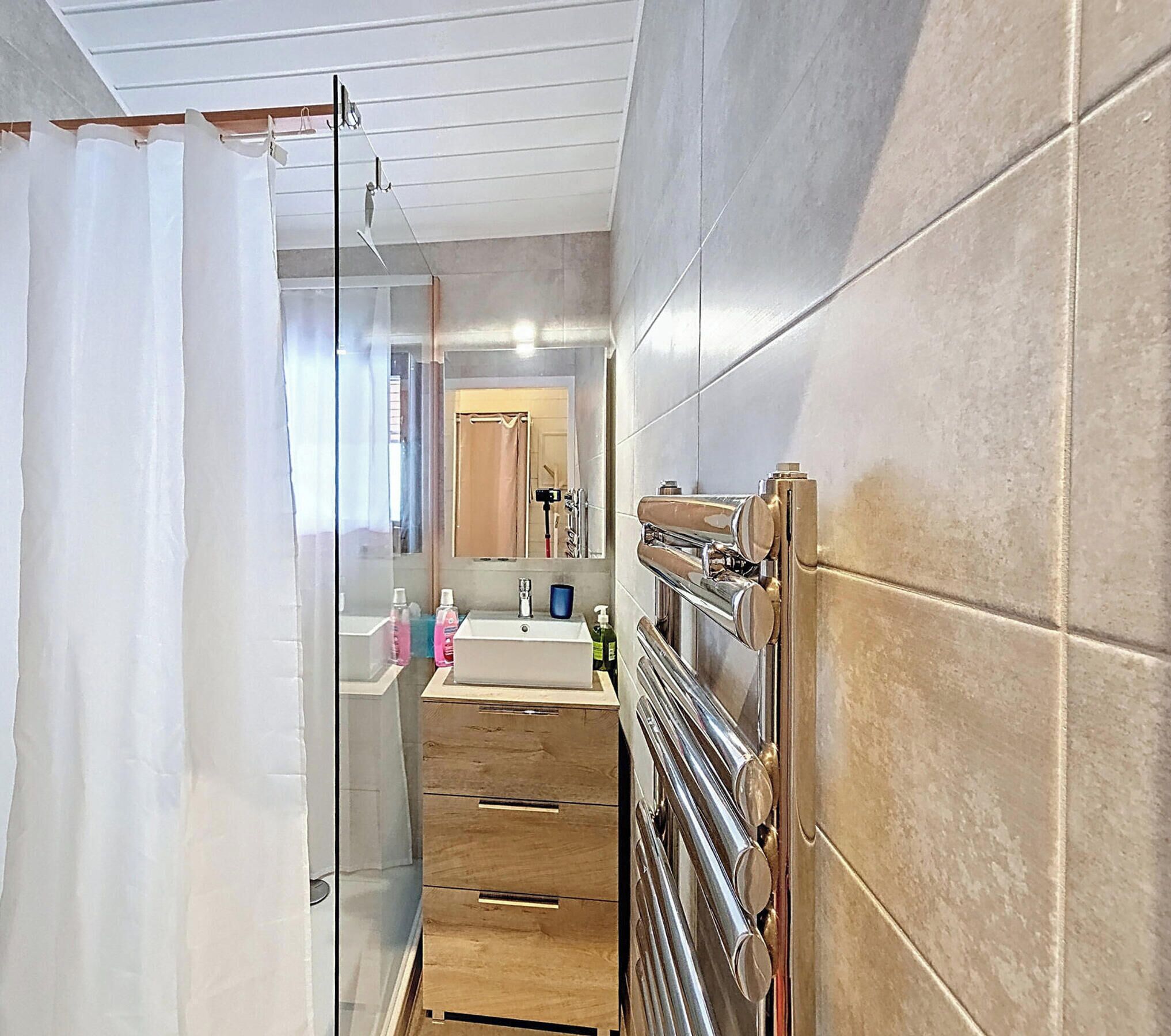 A modern bathroom with a glass shower enclosure, a vanity with a mirror, and a built-in towel rack.