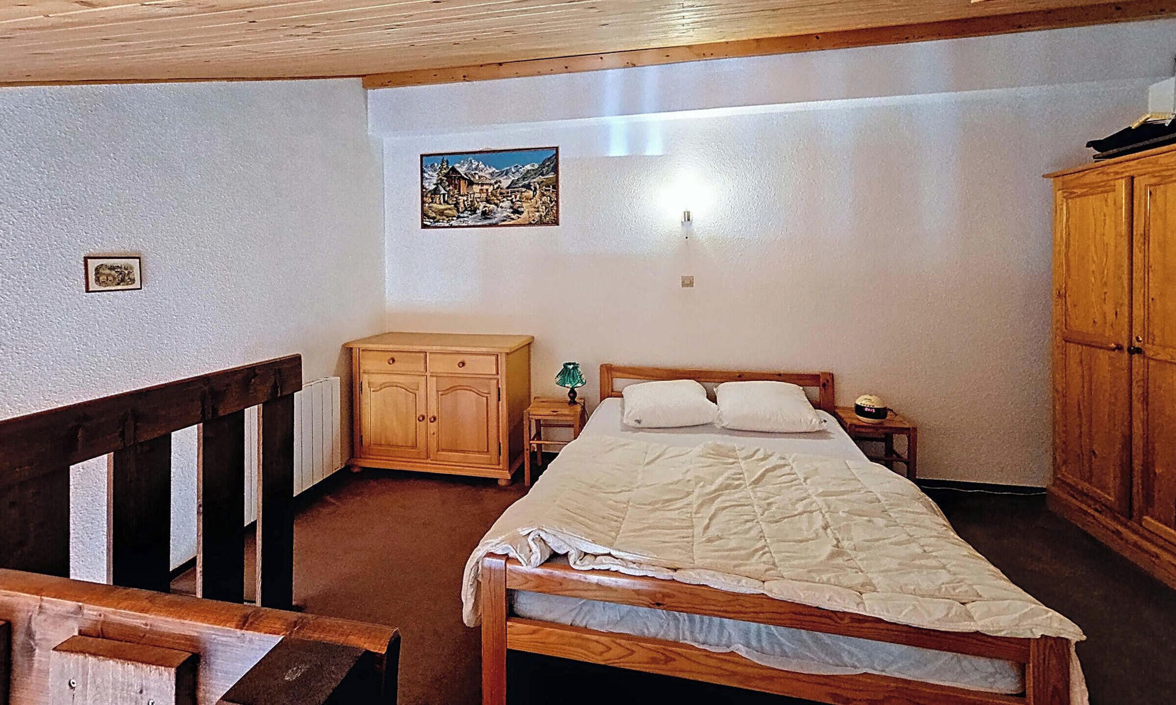A bedroom with a wooden bed, a nightstand, a wooden wardrobe, and a painting on the wall.