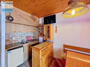 A compact kitchen with wooden cabinets, a tiled backsplash, a small sink, and a stove. There is a television mounted on the wall and a wicker lamp hanging above the counter. - Bright studio with south-facing balcony and parking in La Chapelle-d'Abondance (La Chapelle-d'Abondance)