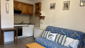 Een compacte leefruimte met een kitchenette, een bank met een gestreept hoesje en een klein houten tafeltje.