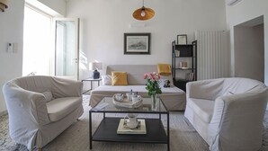 Ett vardagsrum med en soffa, två fåtöljer, ett soffbord, en lampa, en bokhylla och ett fönster.