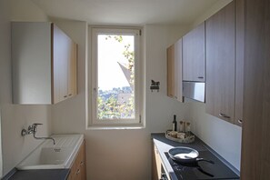 A compact kitchen with a window, a sink, a stove, and wooden cabinets. - Lake Dream House - Apt Private Terrace w/Stunning Isola Comacina (Ossuccio)