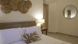 Ett hotellrum med en säng, ett nattduksbord med en lampa, en rund spegel och dekorativ väggkonst.