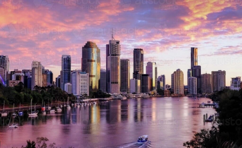 A city skyline with high-rise buildings, a calm river, and a boat moving across the water.