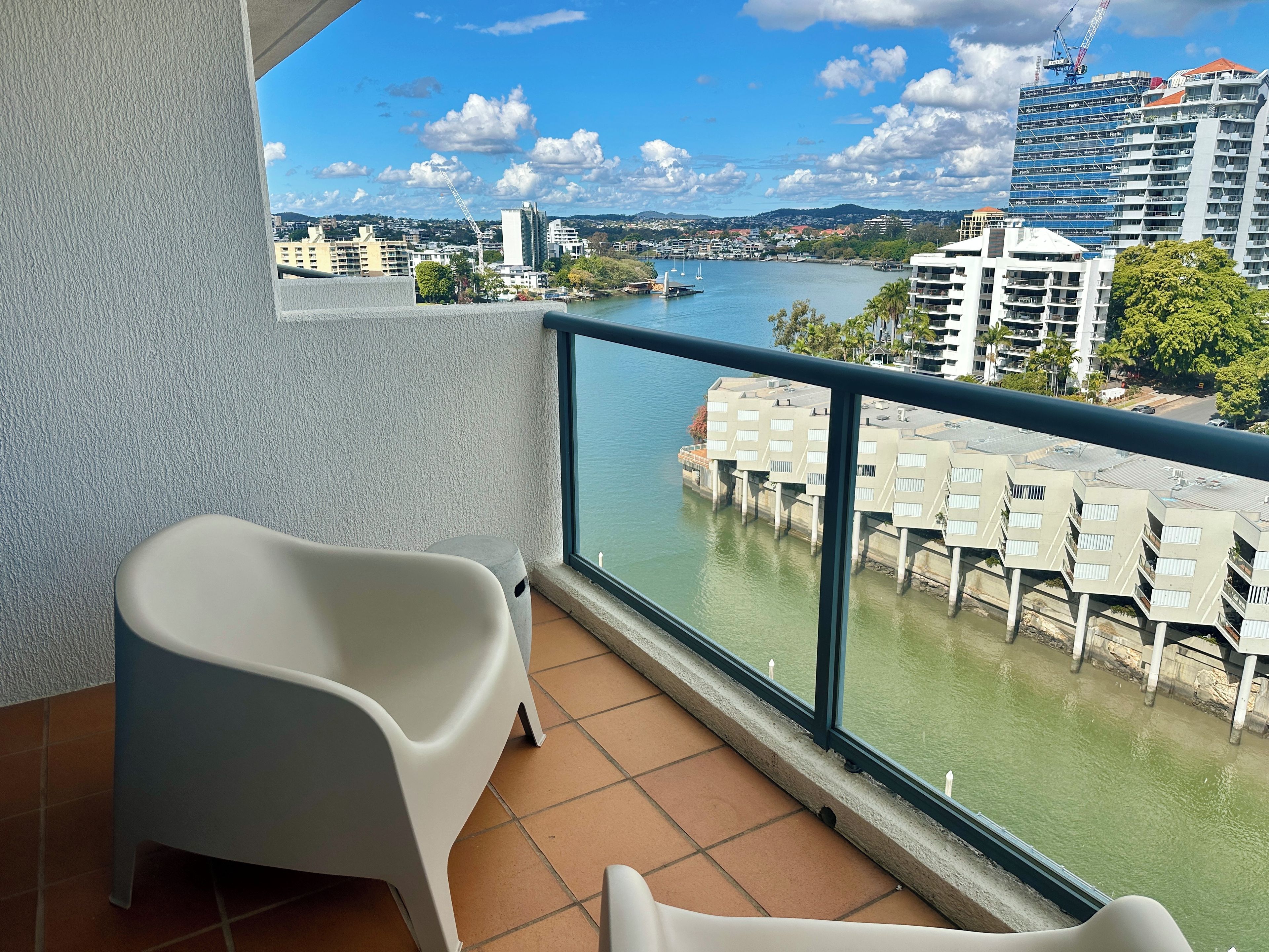 A balcony with a view of a river, a white chair, and a building with a crane in the background.