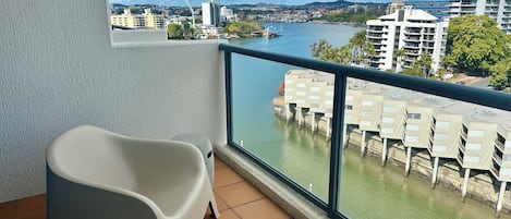 A balcony with a view of a river, a white chair, and a building with a crane in the background.