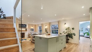 Una cocina moderna con una isla central, suelo de madera y una escalera que sube a un nivel superior.
