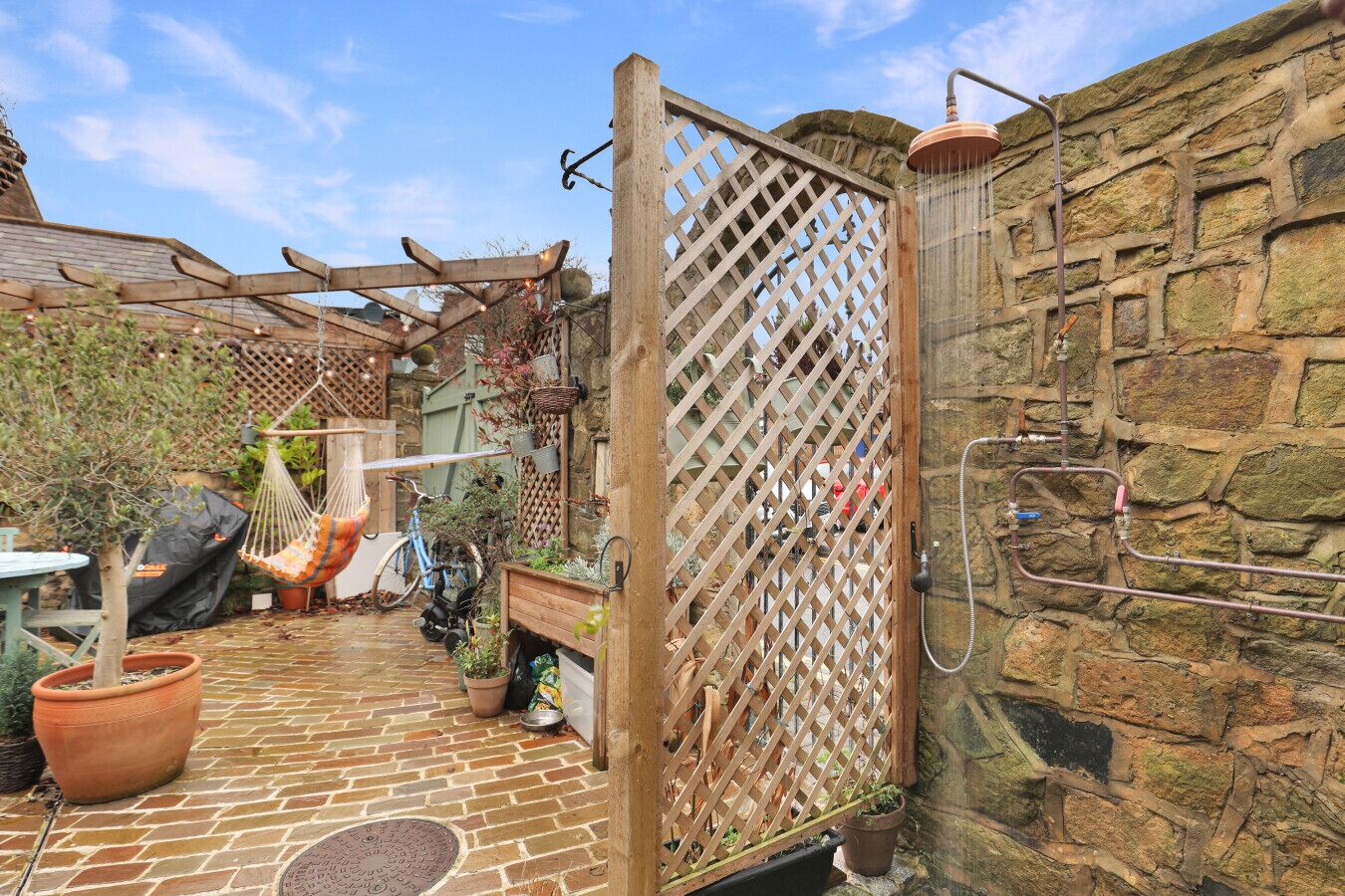 A rustic outdoor area with a brick patio, a hammock, potted plants, and a stone wall.