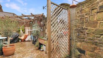 A rustic outdoor area with a brick patio, a hammock, potted plants, and a stone wall.