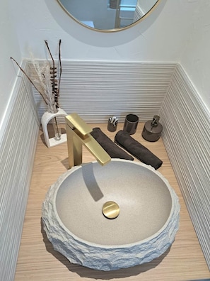 A bathroom with a stone sink, gold fixtures, and a mirror. - To complete (Colmar)