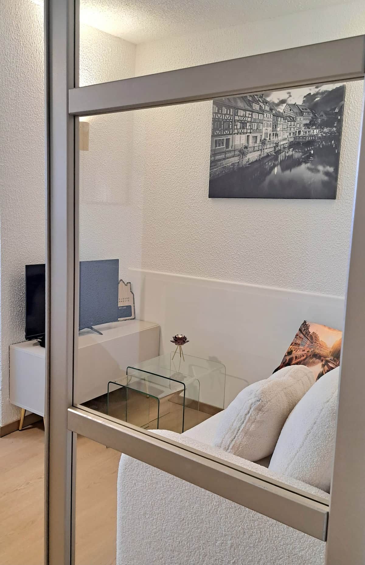Ett modernt vardagsrum med en glasvägg, en soffa, ett soffbord, ett litet sidobord och en inramad tavla på väggen.