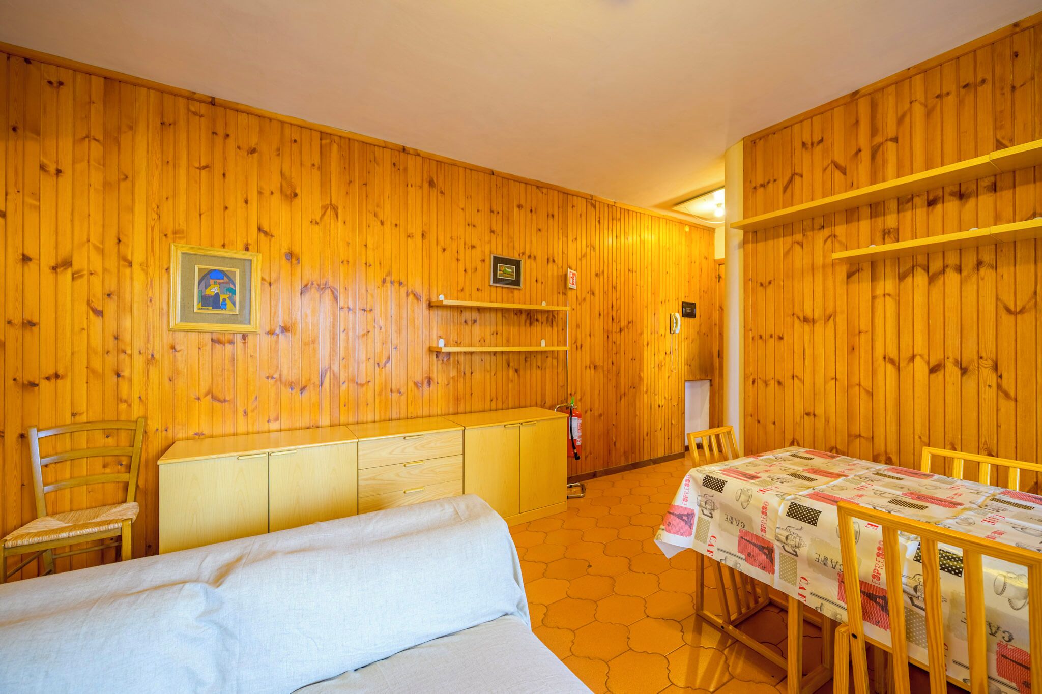 A wooden-paneled room with a bed, a table with a tablecloth, and a chair.