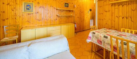 A wooden-paneled room with a bed, a table with a tablecloth, and a chair.