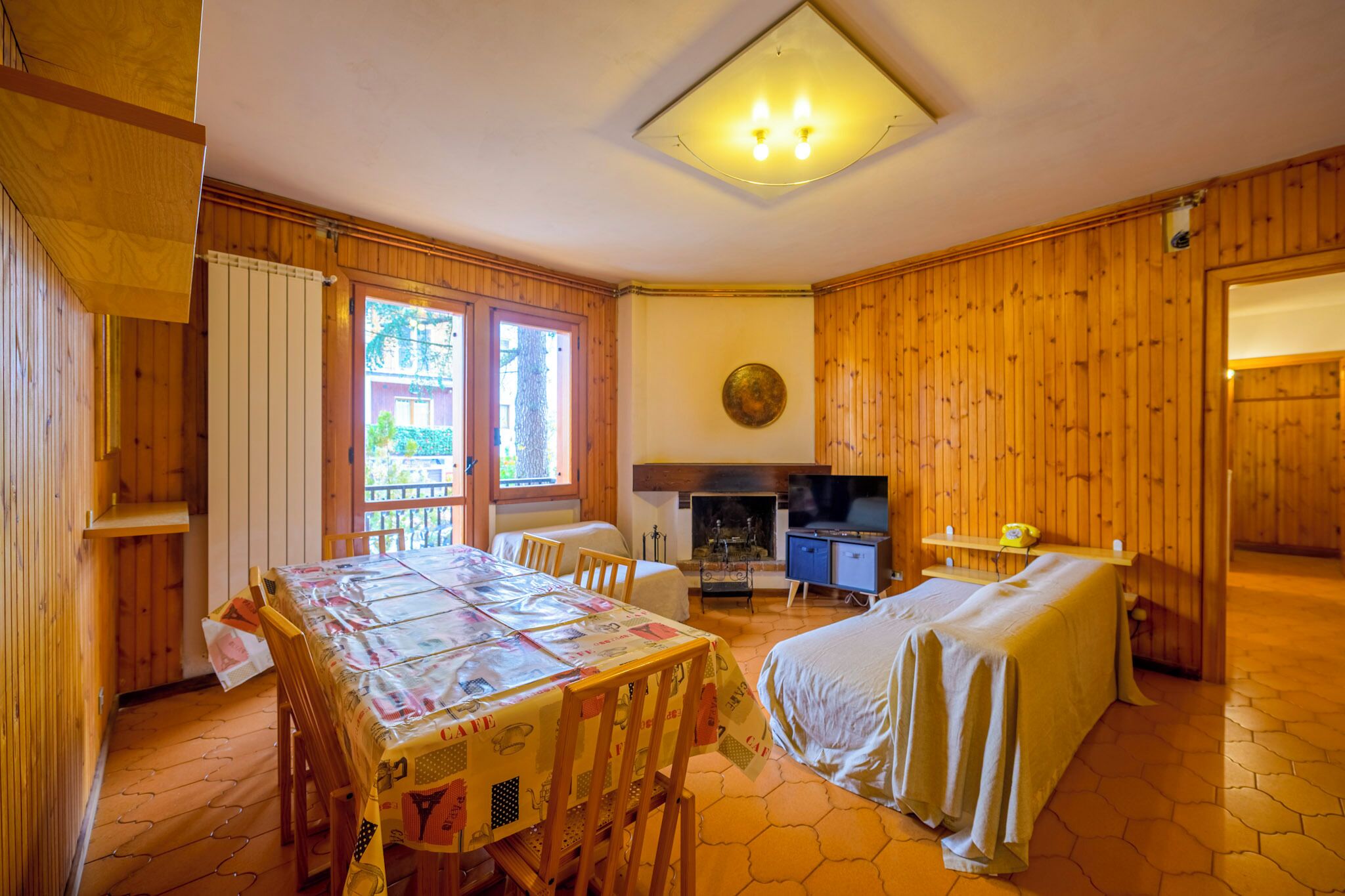 A cozy room with wooden walls, a bed, a dining table with chairs, a TV, and a fireplace.